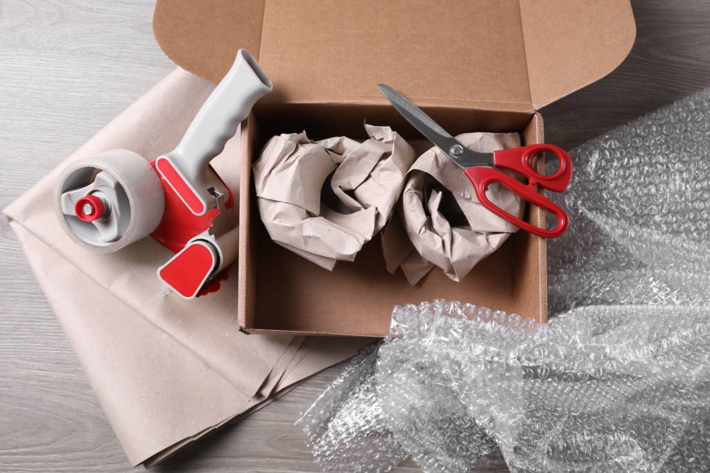 Open box with wrapped items, adhesive tape, scissors, paper and bubble wrap